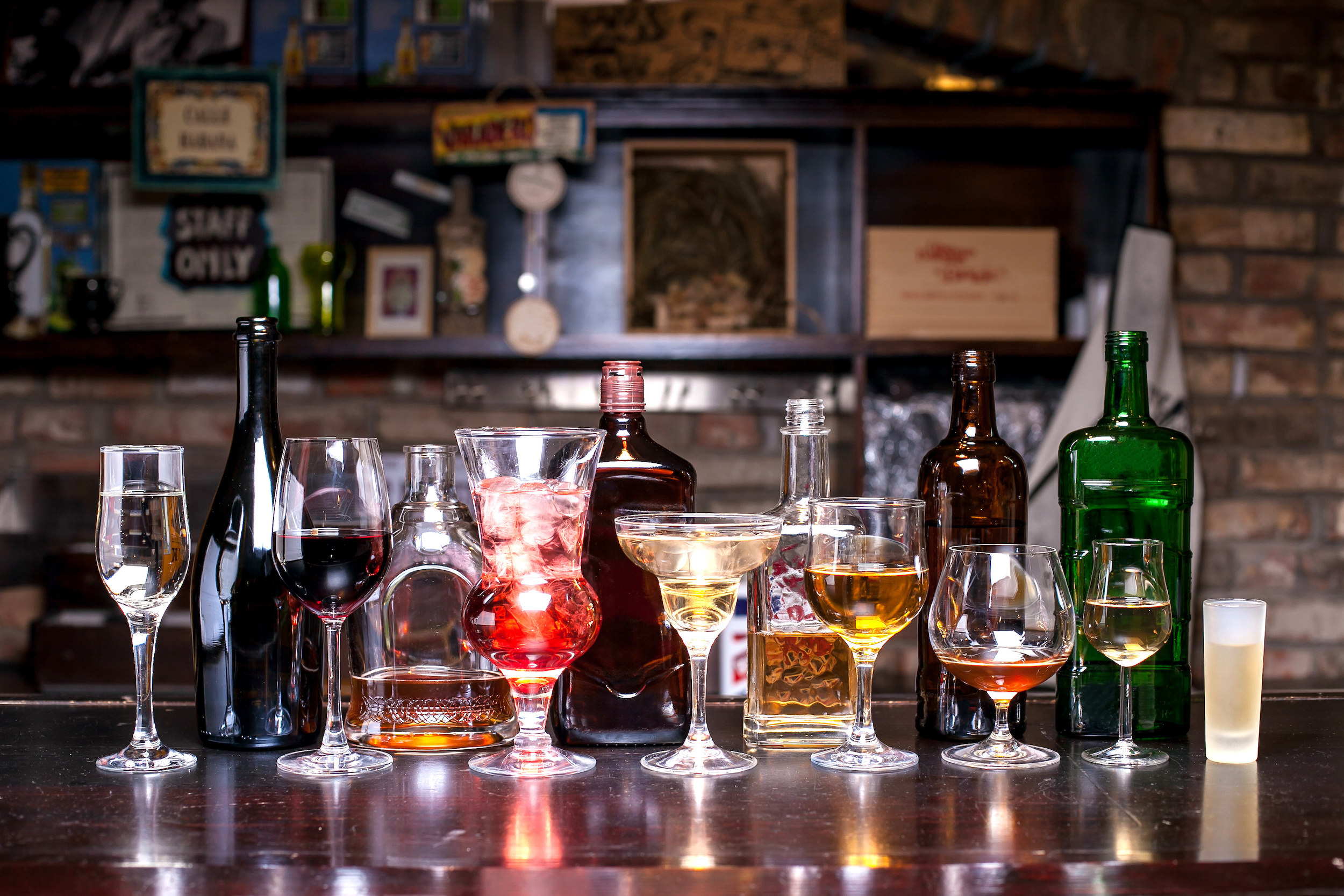 many different bottles of alcohol in different shapes, glasses with alcohol of various shapes, on the bar